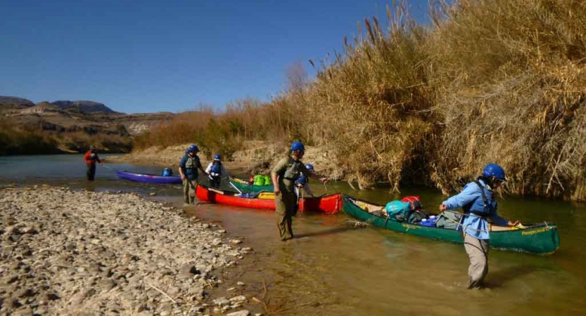 a group of gap year students guide canoes through a shallow portion of water